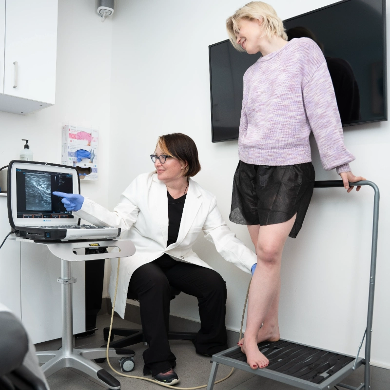 VTC_DrMcKinley_Lifestyle_ (30)-cropped_4672x4672_85q_optimized Dr. Bonnie McKinley performs a Duplex Ultrasound examination on a patient's leg to evaluate for Varicose Veins and Venous Reflux. The patient stands on an examination platform while the provider operates the ultrasound probe to visualize venous structures in a clinical setting.